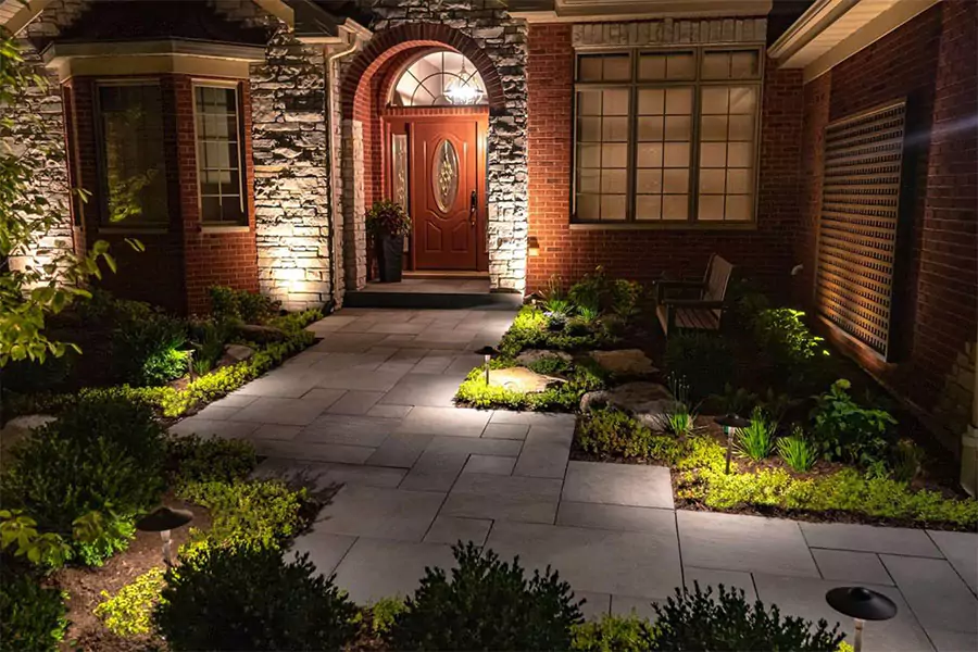 Elegant front yard with beautifully designed landscape lighting illuminating the pathway and greenery, creating a warm and inviting ambiance at night.