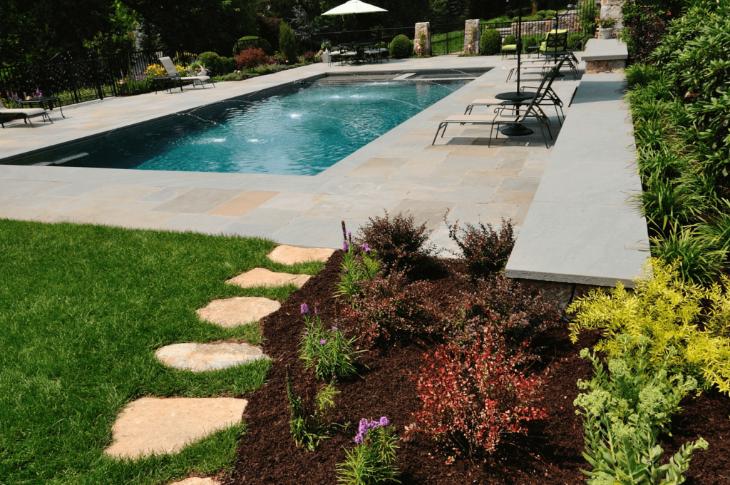 Luxury pool landscaping with stone patio, vibrant flower beds, and stepping stone pathway surrounded by lush green lawn