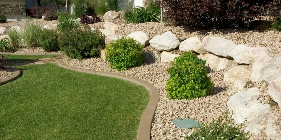 Low-maintenance xeriscape landscaping with decorative rock bed, curved lawn edge, drought-tolerant plants, and large natural boulders