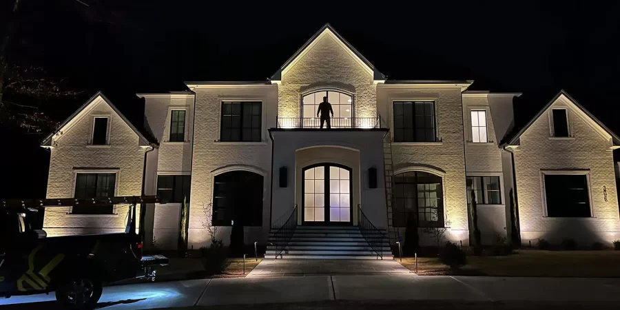 Two-story white brick home with accent lighting highlighting the entryway and windows.